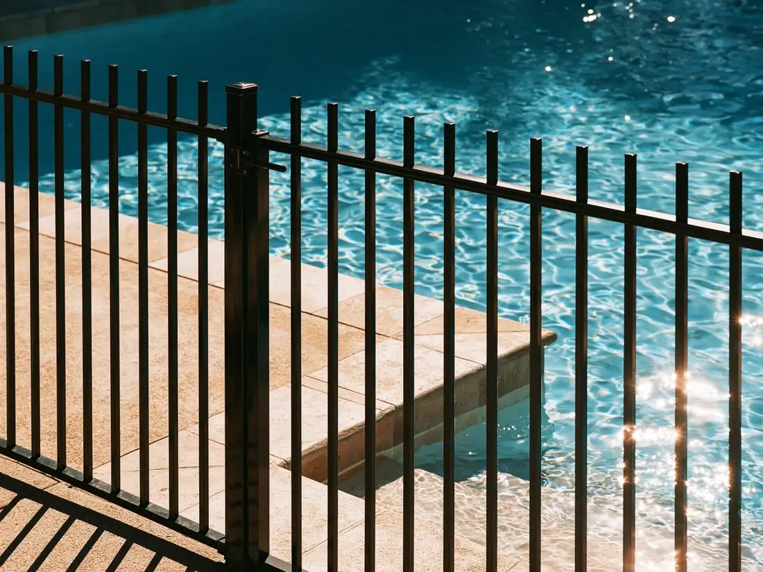 Close view of a black iron pool fence in Tempe, AZ, the pickets plumb and evenly spaced with sunlit pool water behind